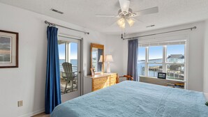 Ein Schlafzimmer mit Bett, Schminktisch, Sessel, Fenster mit Aussicht und Deckenventilator.