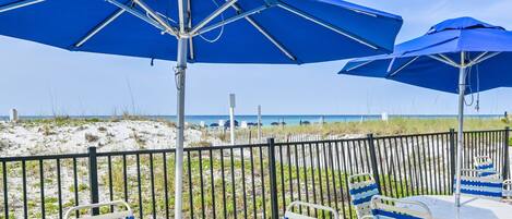 A beachside patio with blue umbrellas, white tables, and striped chairs.