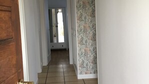 Ein Flur mit Holztür, Fliesenboden und Wand mit Muster, sowie einer hängenden Leuchte.