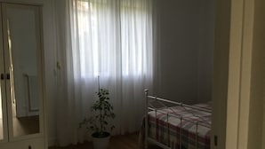 Ein Schlafzimmer mit einem Einzelbett, einer Topfpflanze, einem Kleiderschrank und einem Fenster mit durchscheinenden Vorhängen.