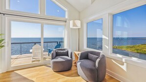 Ett rymligt rum med stora fönster med utsikt över havet, inrett med två grå fåtöljer och ett litet bord.
