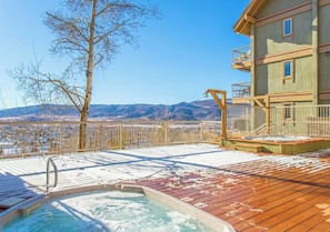 A wooden deck with a hot tub, a wooden building with balconies, and a view of mountains.