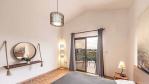 Un dormitorio con cama, un espejo colgado, una mesita de noche con lámpara y vistas al exterior a través de una puerta corredera.