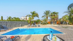 Una piscina con sillas de descanso, un muro de piedra y palmeras.