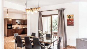 Una cocina moderna con armarios de madera oscura, horno integrado y comedor con mesa de vidrio y sillas negras.