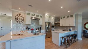 A modern kitchen with white cabinetry, a central island with stools, stainless steel appliances, and a decorative clock. - Designer Ranch w/Gourmet Kitchen and Downtown Views. (Paso Robles)