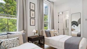 A bedroom with two beds, a nightstand, a mirror, and a window with curtains.