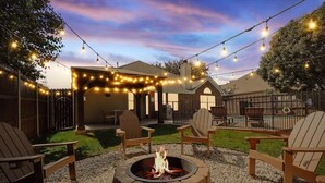 A backyard with a fire pit, outdoor seating, and string lights.