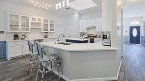 A modern kitchen with white cabinetry, a central island with seating, and a dining area with wicker chairs.
