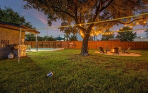 Um quintal com piscina, área de churrasco e uma árvore com luzes de cordão.