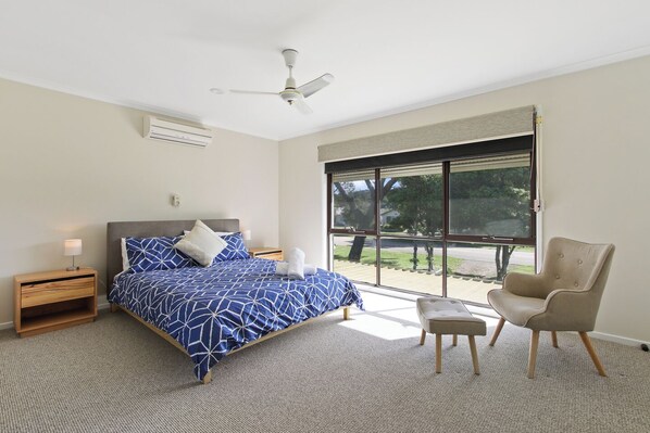 Un dormitorio con cama, mesita de noche, silla, ventilador de techo y un ventanal con vistas al exterior.