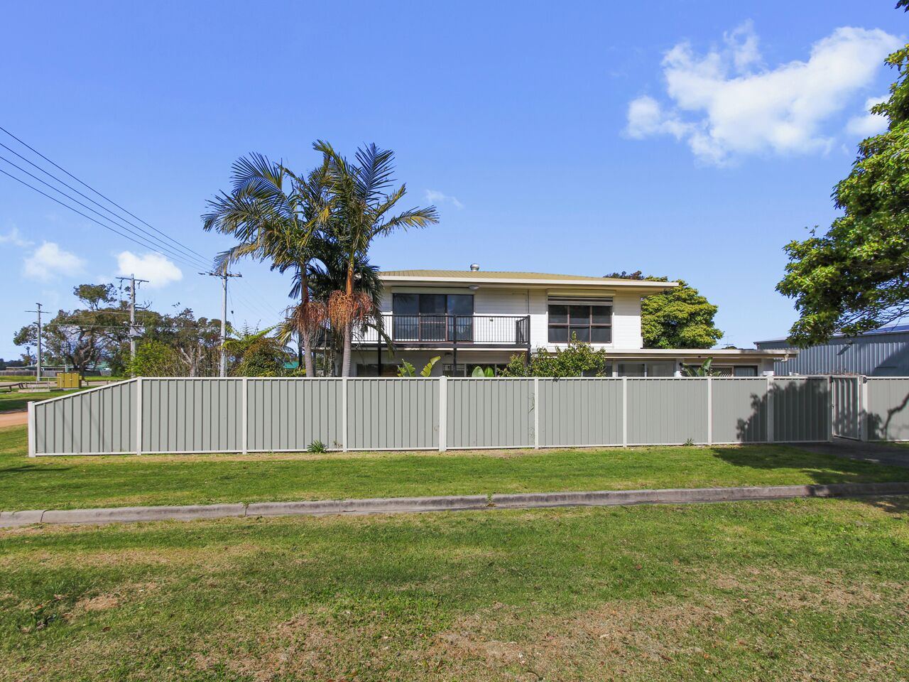 A residential area with a two-story house, a fenced yard, and a palm tree.