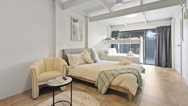 Ein Schlafzimmer mit Etagenbett, Einzelbett, Stuhl, kleinem Tisch und Deckenventilator.
