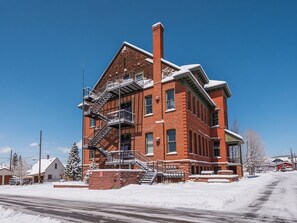 A red brick building with a fire escape, a large chimney, and a snow-covered roof. - Modern 2BR Loft: Walk to Downtown - 30 plus day (Leadville)