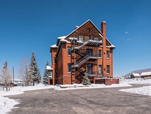 A red brick building with a fire escape, surrounded by snow-covered trees and a clear sky. - Modern 2BR Loft: Walk to Downtown - 30 plus day (Leadville)