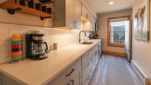 A modern kitchen with white cabinets, a coffee maker, and a window with a view of the outdoors. - Sundowner II Treeline Condo: Ski-In, Walk To Town/Lift (Breckenridge)