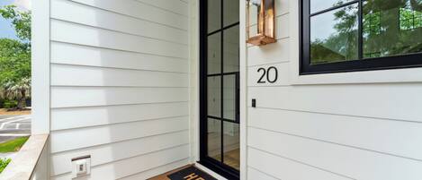 A white house with a black-framed door, a number '20' above the door, and a 'HELLO' mat at the entrance.