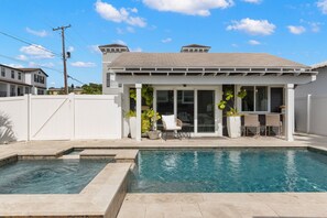 A residential property with a swimming pool, a covered patio with seating, and a white fence.