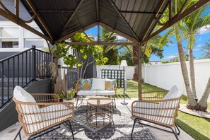 Un área de estar al aire libre cubierta, con muebles de mimbre y un tapiz estampado.