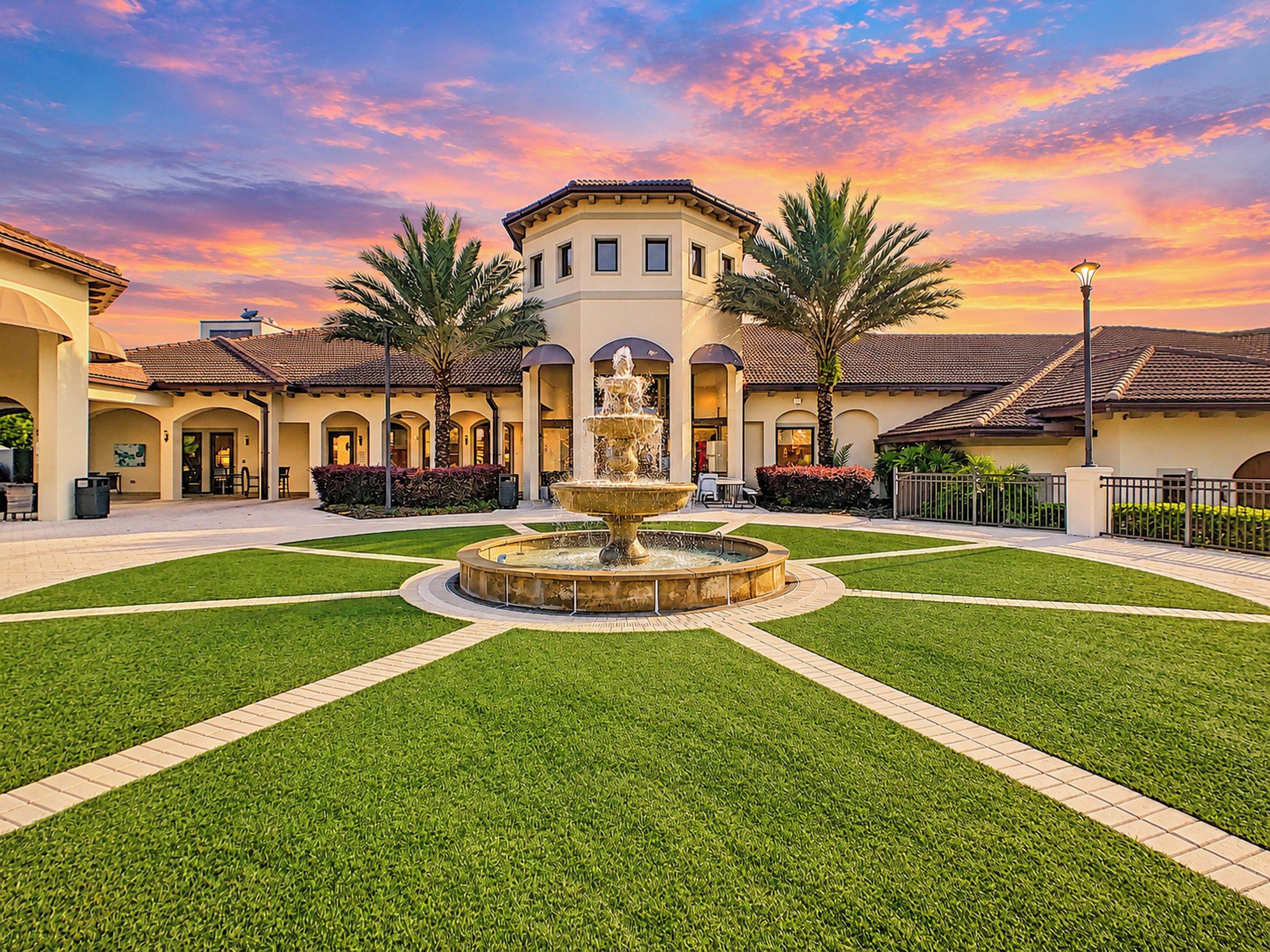 A courtyard with a central fountain, surrounded by palm trees and a building with arched doorways.