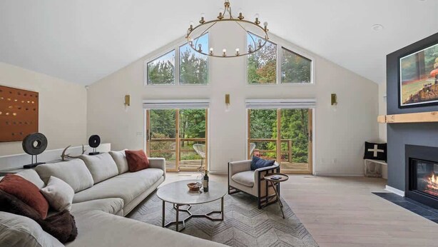A spacious loft with a high ceiling, large windows, a fireplace, and a modern chandelier.