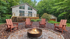 A cabin with a deck, a fire pit, and Adirondack chairs.
