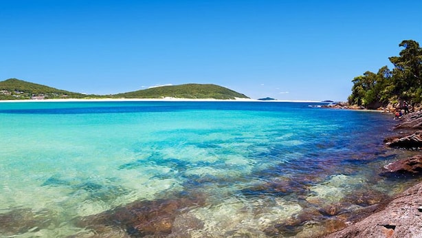 A beach with clear turquoise water, rocky shoreline, and distant green hills. - Fingal Bay Panorama - Panoramic Ocean Views, 300m to Beach with Pool Table (Fingal Bay)