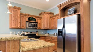 A kitchen with wooden cabinets, a stainless steel refrigerator, a microwave, and a granite countertop. - Sleeps 6 in a 4plex w Pool, Only a Block to Beach (South Padre Island)
