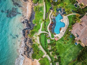 Luftaufnahme eines Resorts mit großem Schwimmbecken, Strandbereich und üppiger Vegetation.