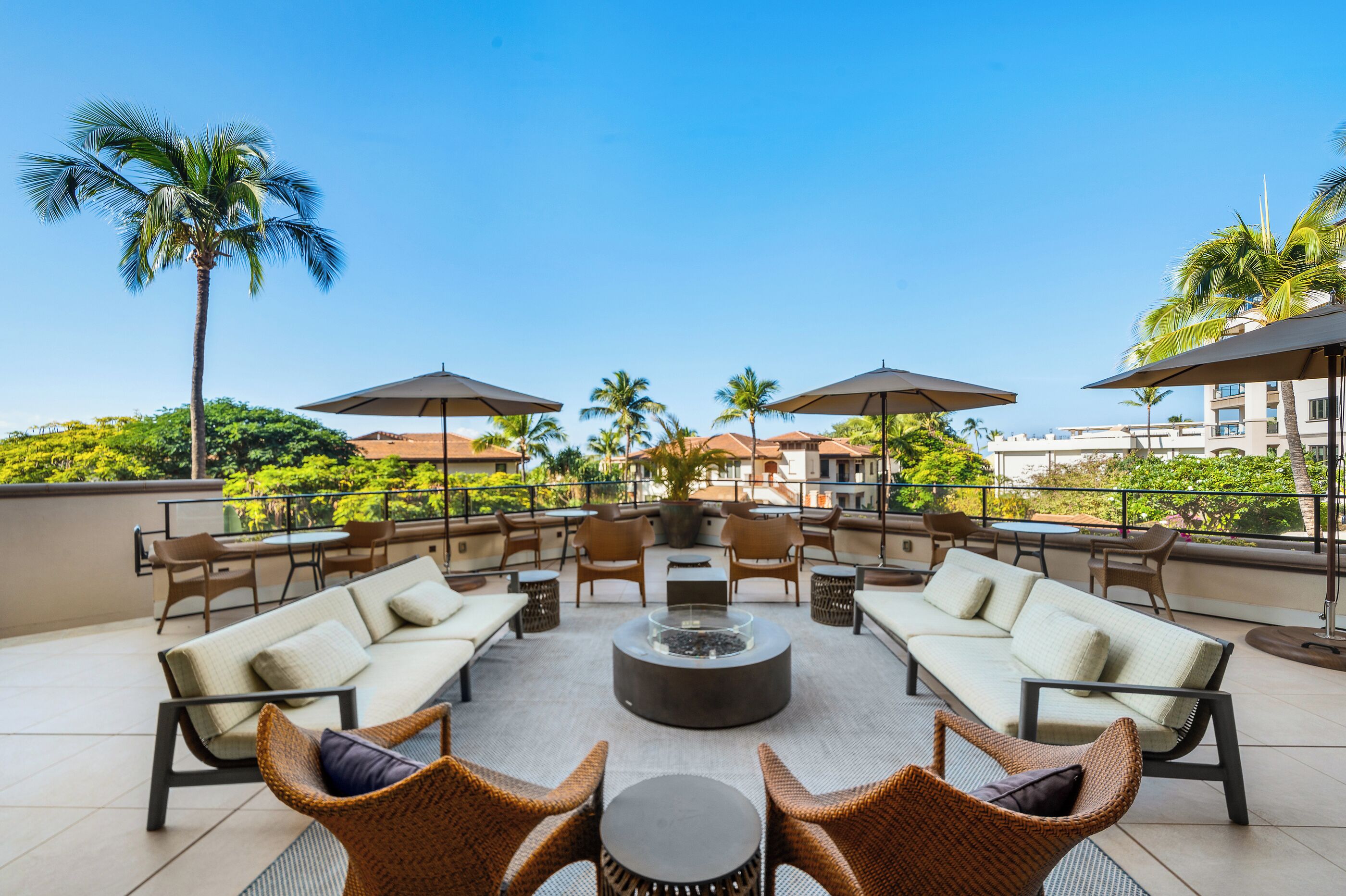 A rooftop terrace with outdoor seating, a fire pit, and palm trees.