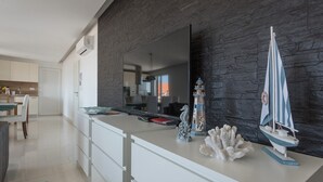 Una cucina moderna con zoccolo nero in pietra, mobili bianchi e un grande specchio sopra il piano di lavoro. Elementi decorativi: una riproduzione di un faro e una barca a vela.