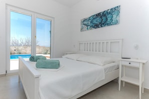 A bedroom with a bed, a bedside table, and a view of a swimming pool.