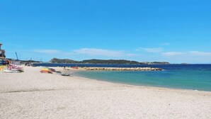 Ein Strand mit einer steinernen Wellenbrecheranlage, klarem blauen Wasser und einem Sandstrand.