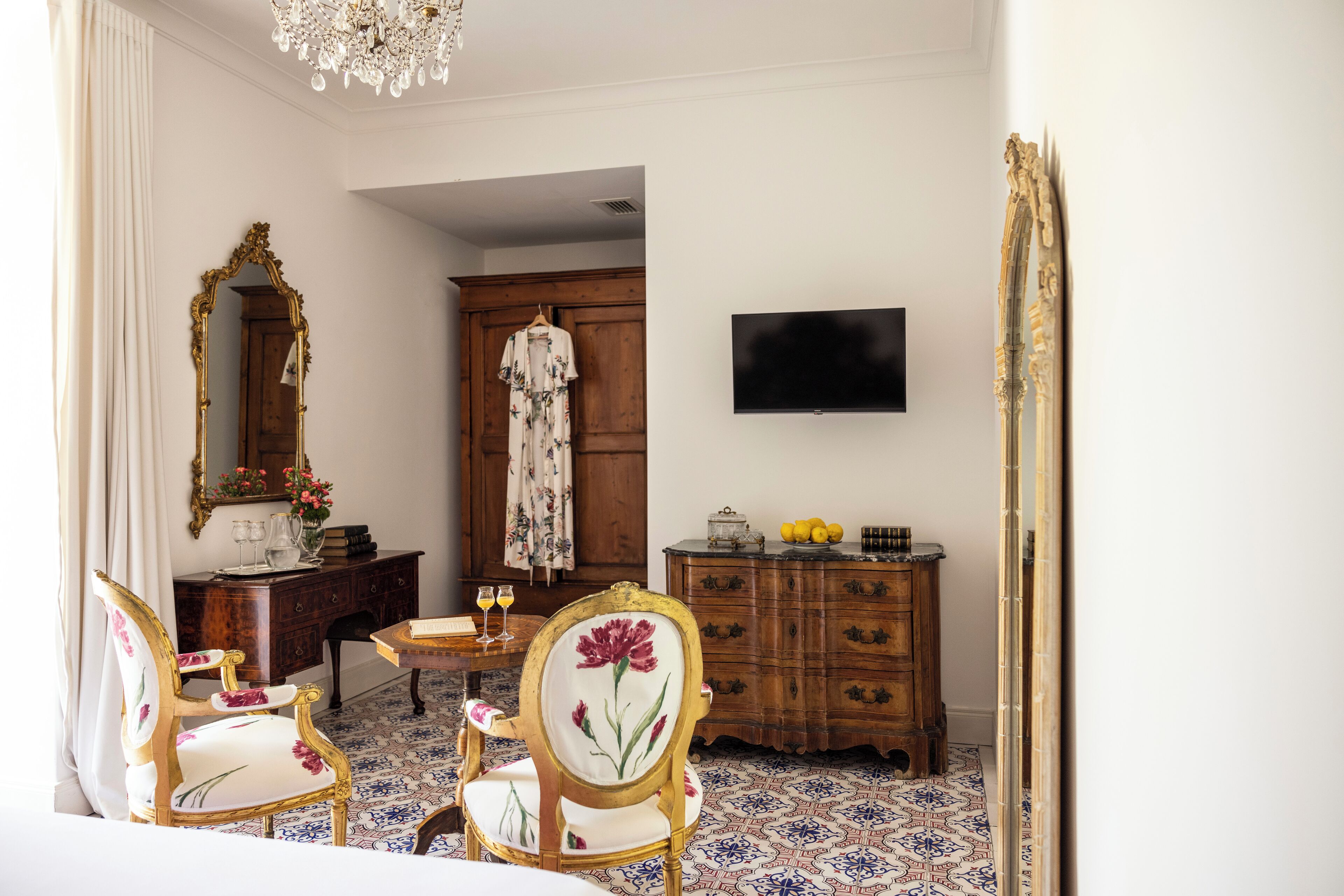 Una habitación con un aparador de madera, un televisor instalado en la pared y una silla con tapicería floral.