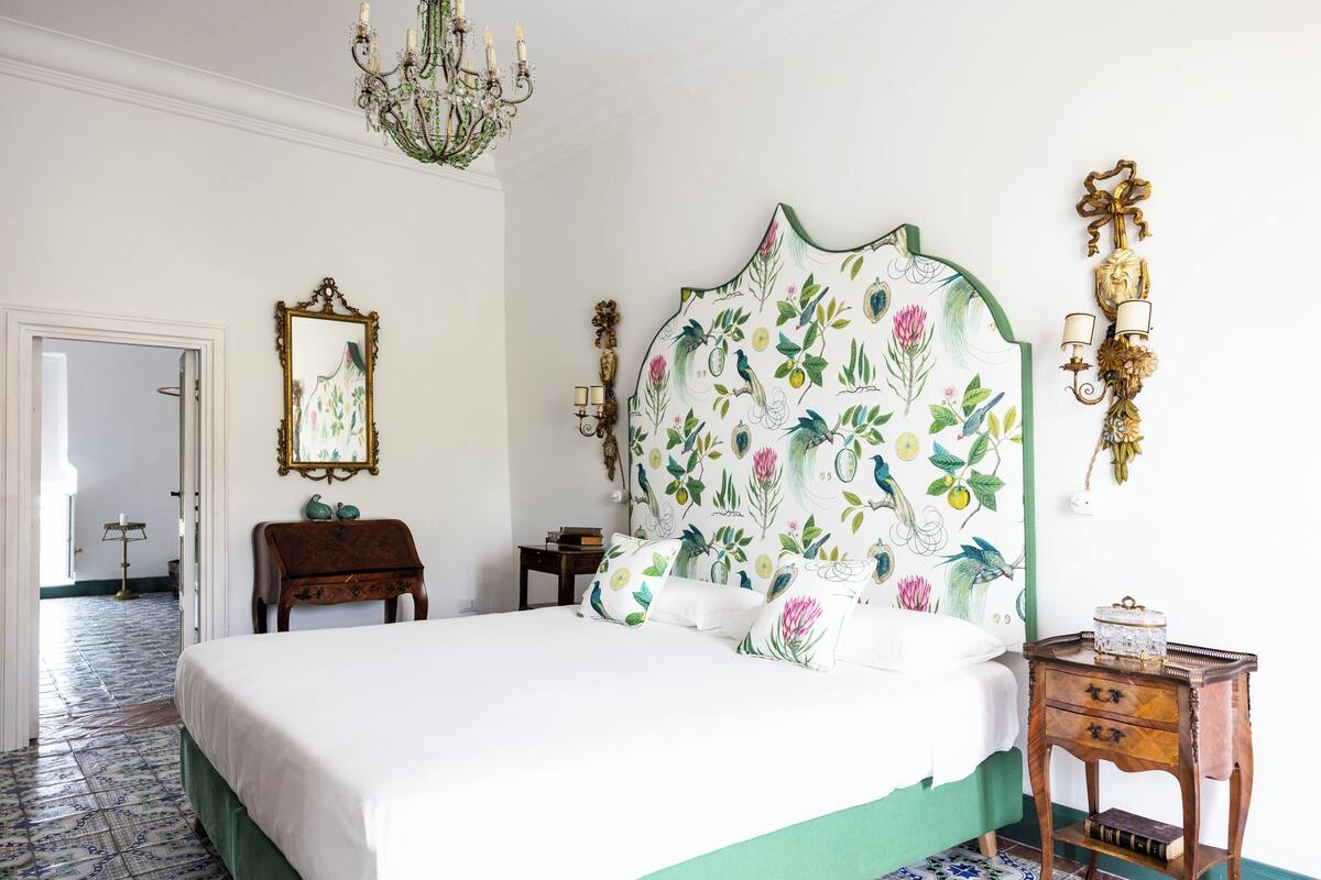 Un dormitorio con una cama grande, una mesita de noche de madera, un espejo y una araña.