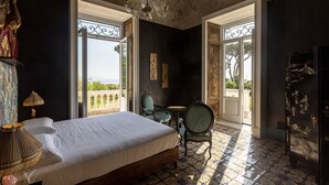 A bedroom with a large bed, a chandelier, a small table with chairs, and a view of the outdoors. - Villa De Cillis Carafa (Torre del Greco)
