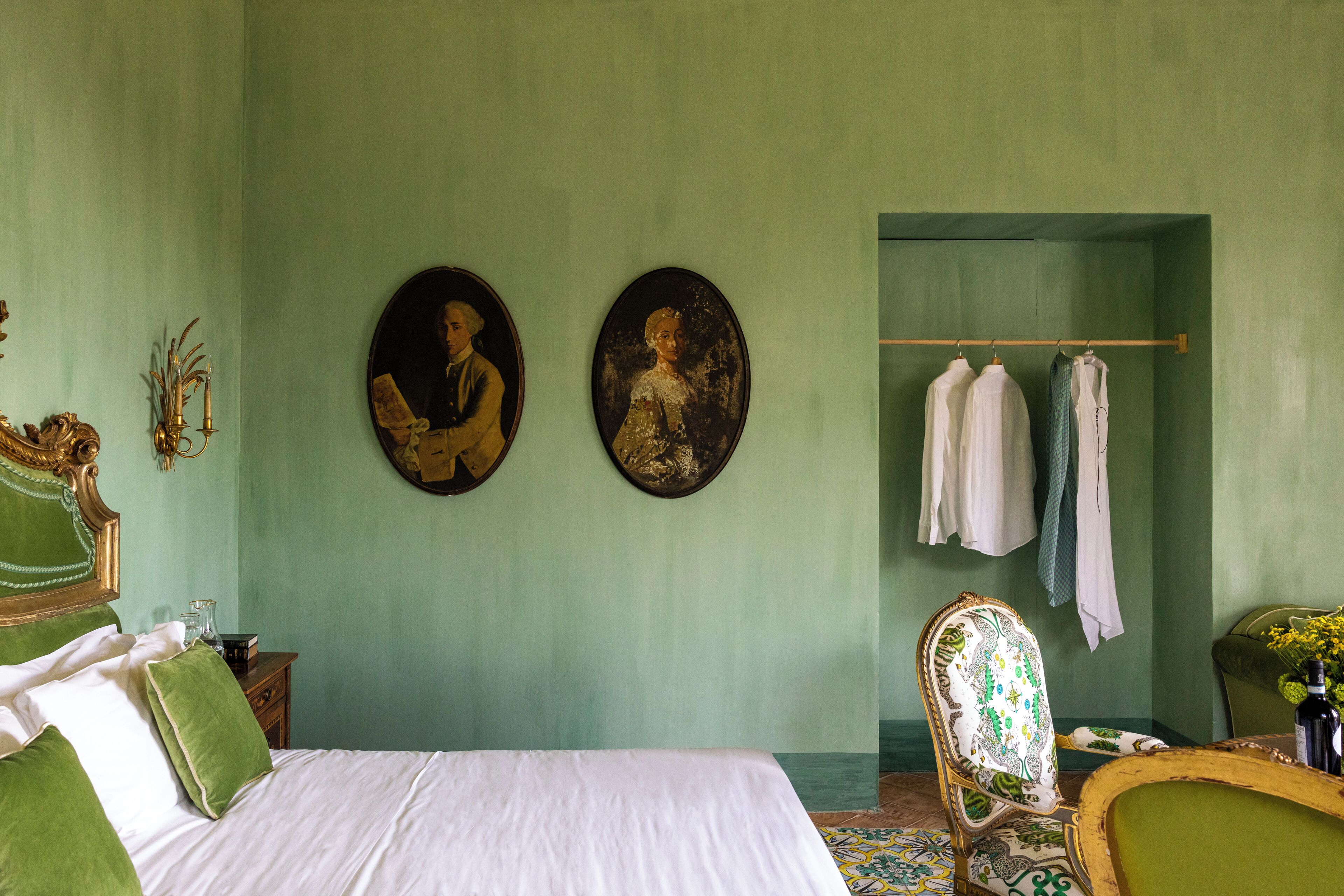 Una habitación con una cama, dos cuadros ovalados, una silla y un perchero.