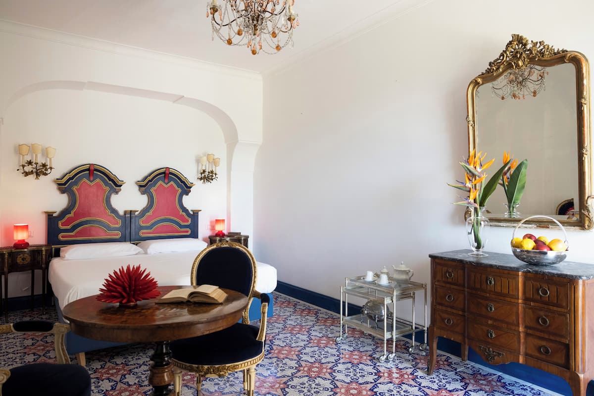 Habitación de hotel con cama, una mesa redonda de madera, una silla, un aparador, un espejo y una araña.