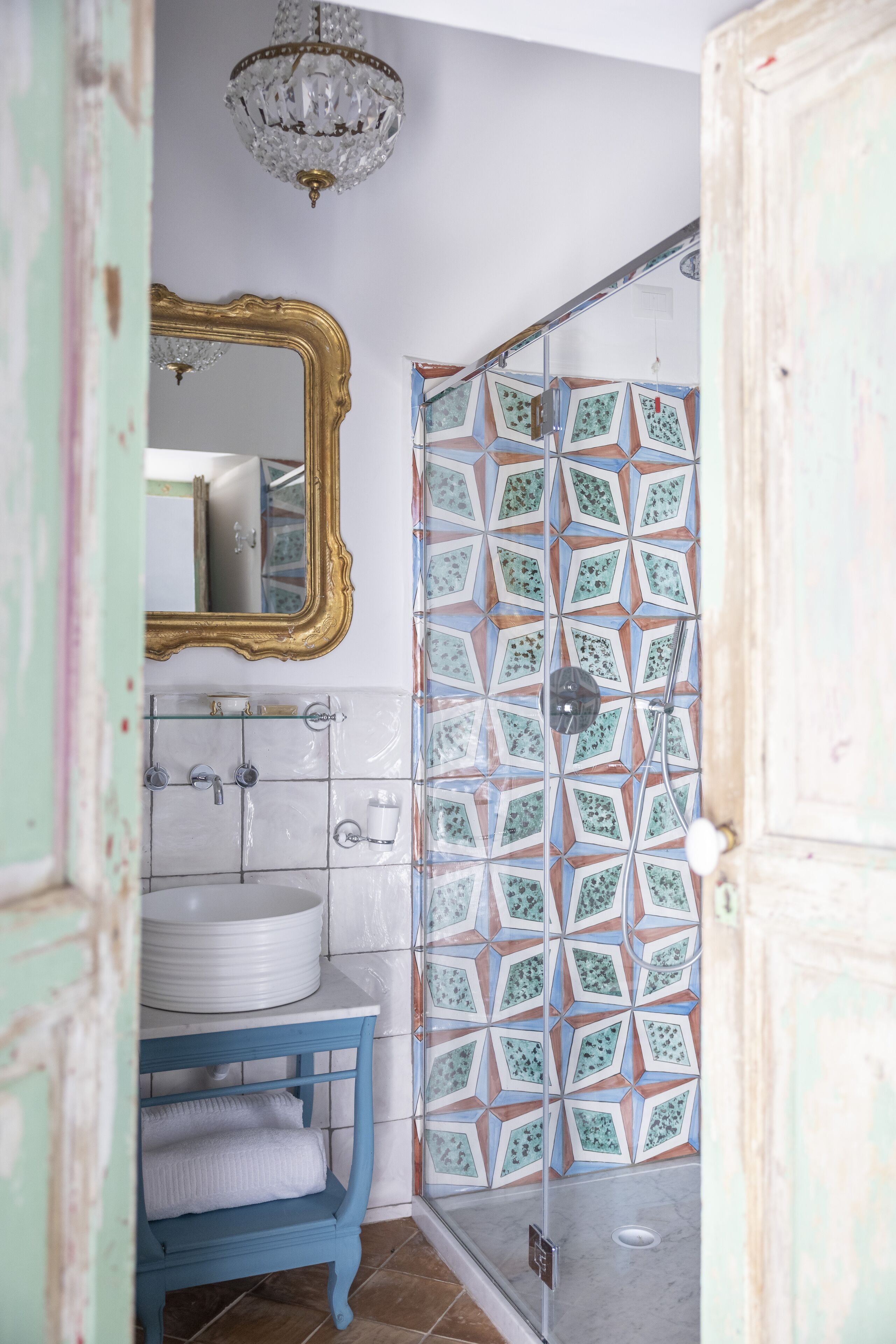 A bathroom with a white sink, blue vanity, and a shower with patterned tiles.
