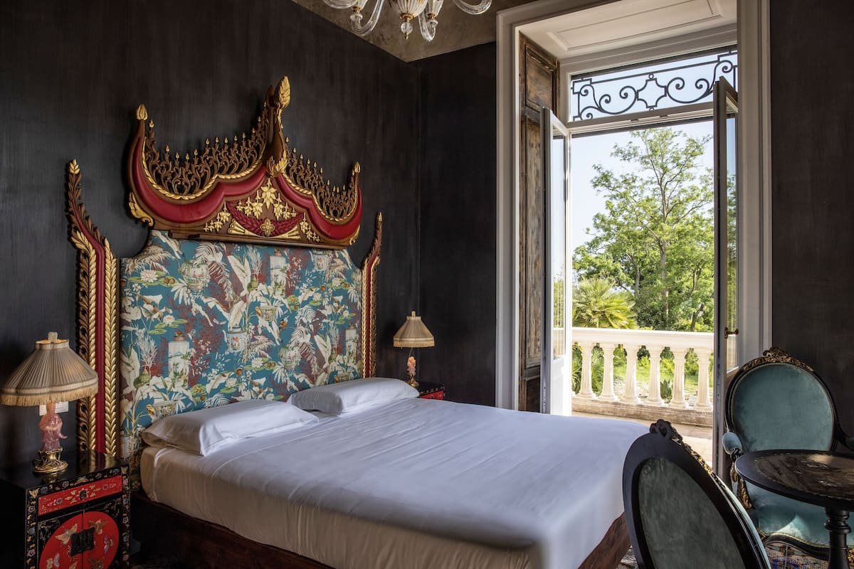 Un dormitorio con una cama grande, un cabecero decorativo y un balcón con barandilla.