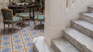 A grand staircase with white balustrades leading to an upper floor. A round table with chairs and decorative items is positioned at the base of the stairs. - Villa De Cillis Carafa (Torre del Greco)