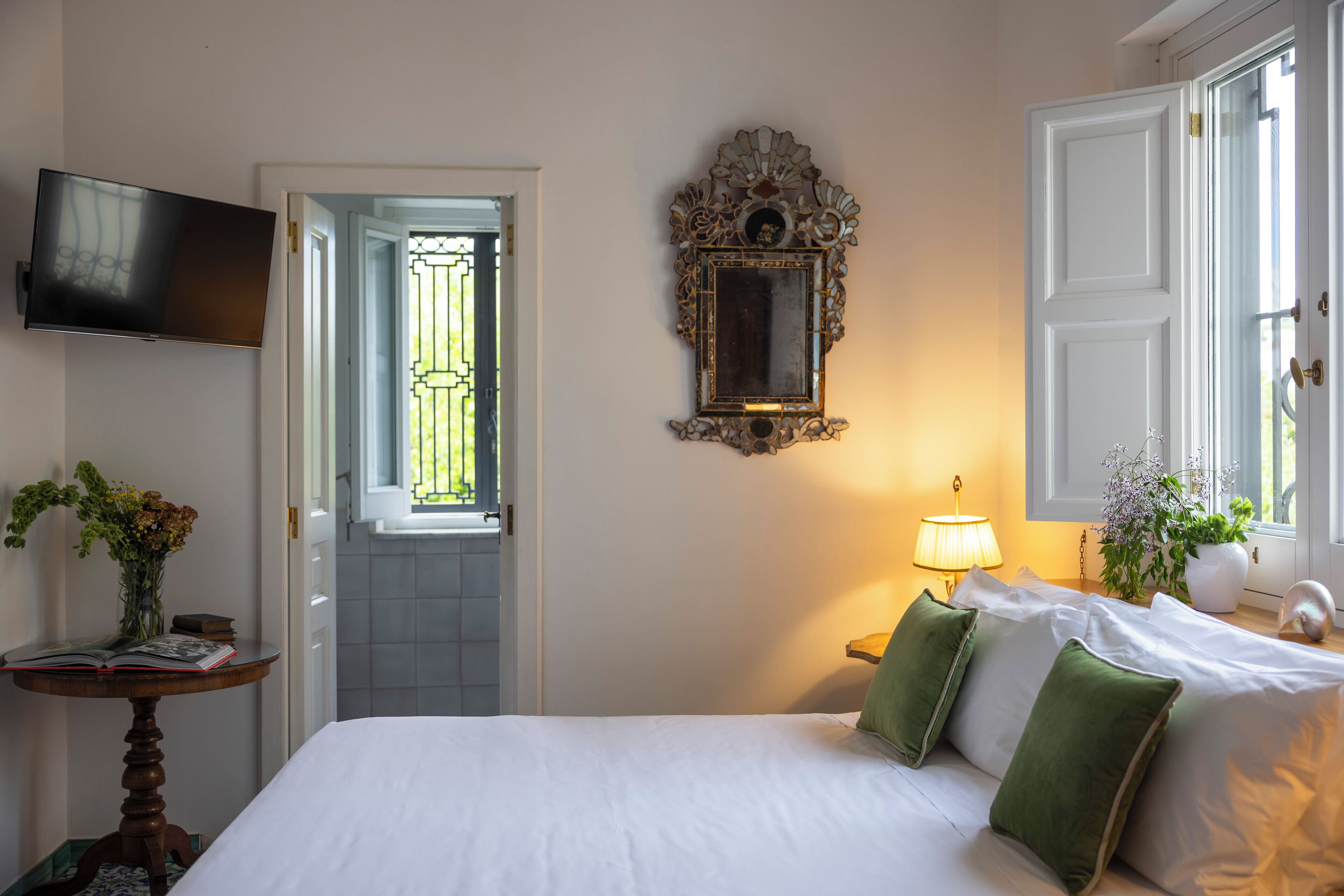 A hotel room with a bed, a television, a mirror, a lamp, and a door leading to a balcony.