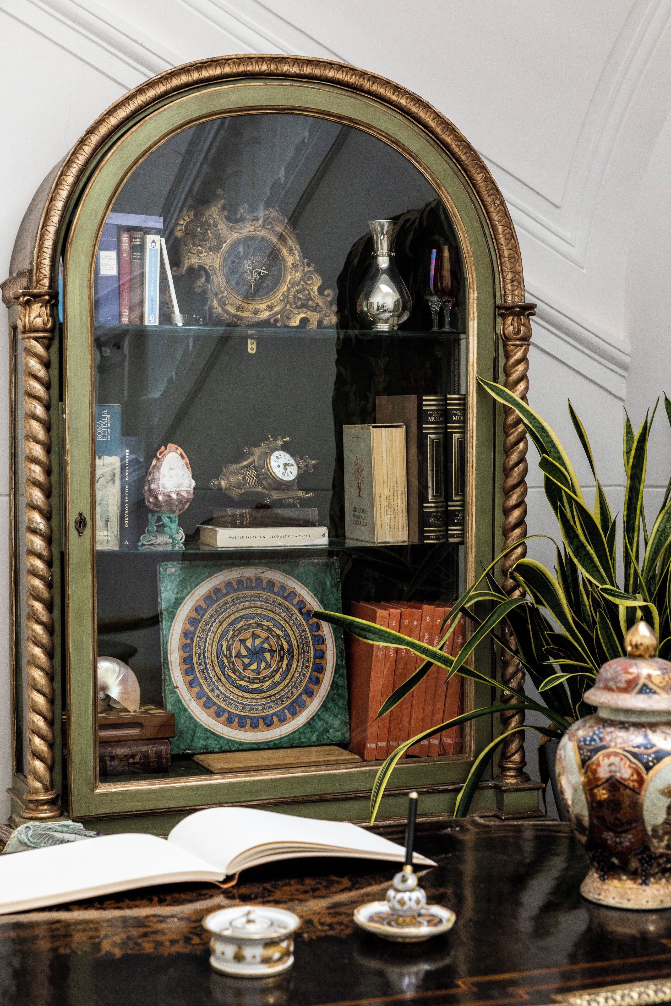 A mirror with an ornate frame, a book, a vase, and a plant on a wooden table.