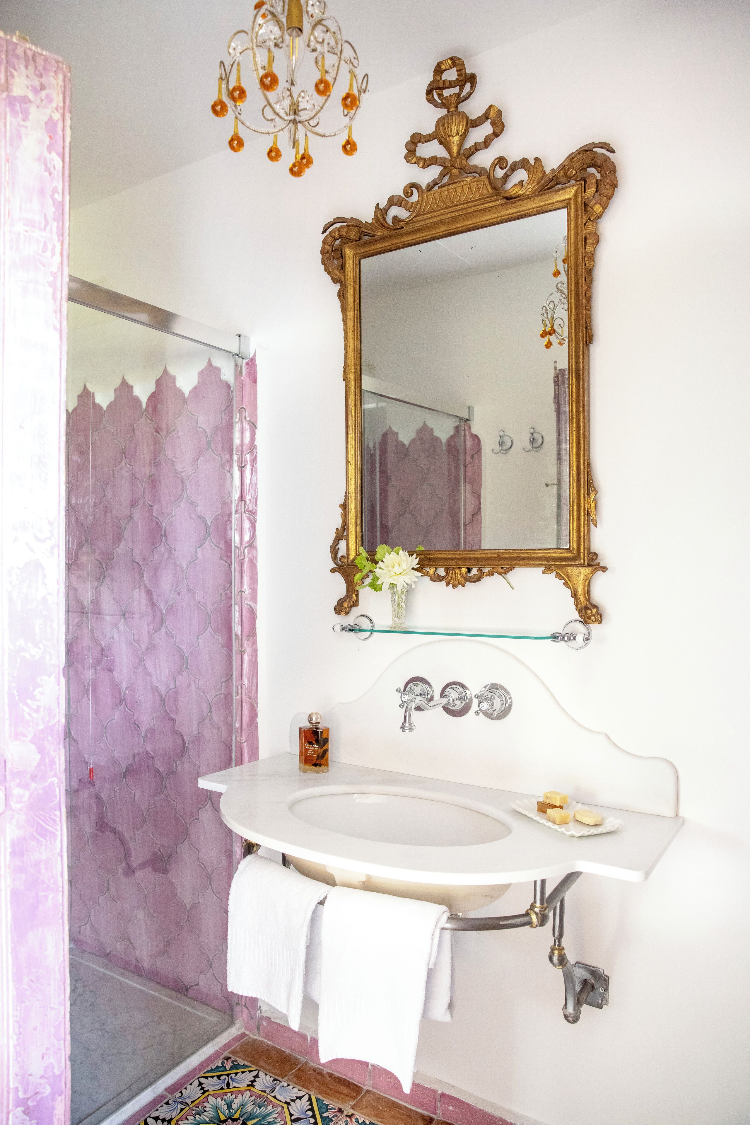Un baño con un lavamanos blanco, espejo con marco dorado y cortina de ducha.