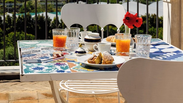 A table set with breakfast items and drinks, overlooking a scenic view of the sea and mountains. - Villa De Cillis Carafa (Torre del Greco)
