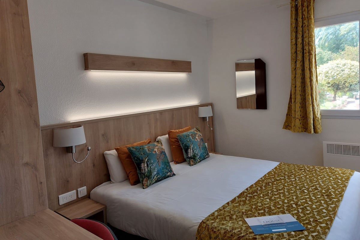 A hotel room with a bed, bedside lamps, a mirror, and a window with curtains.