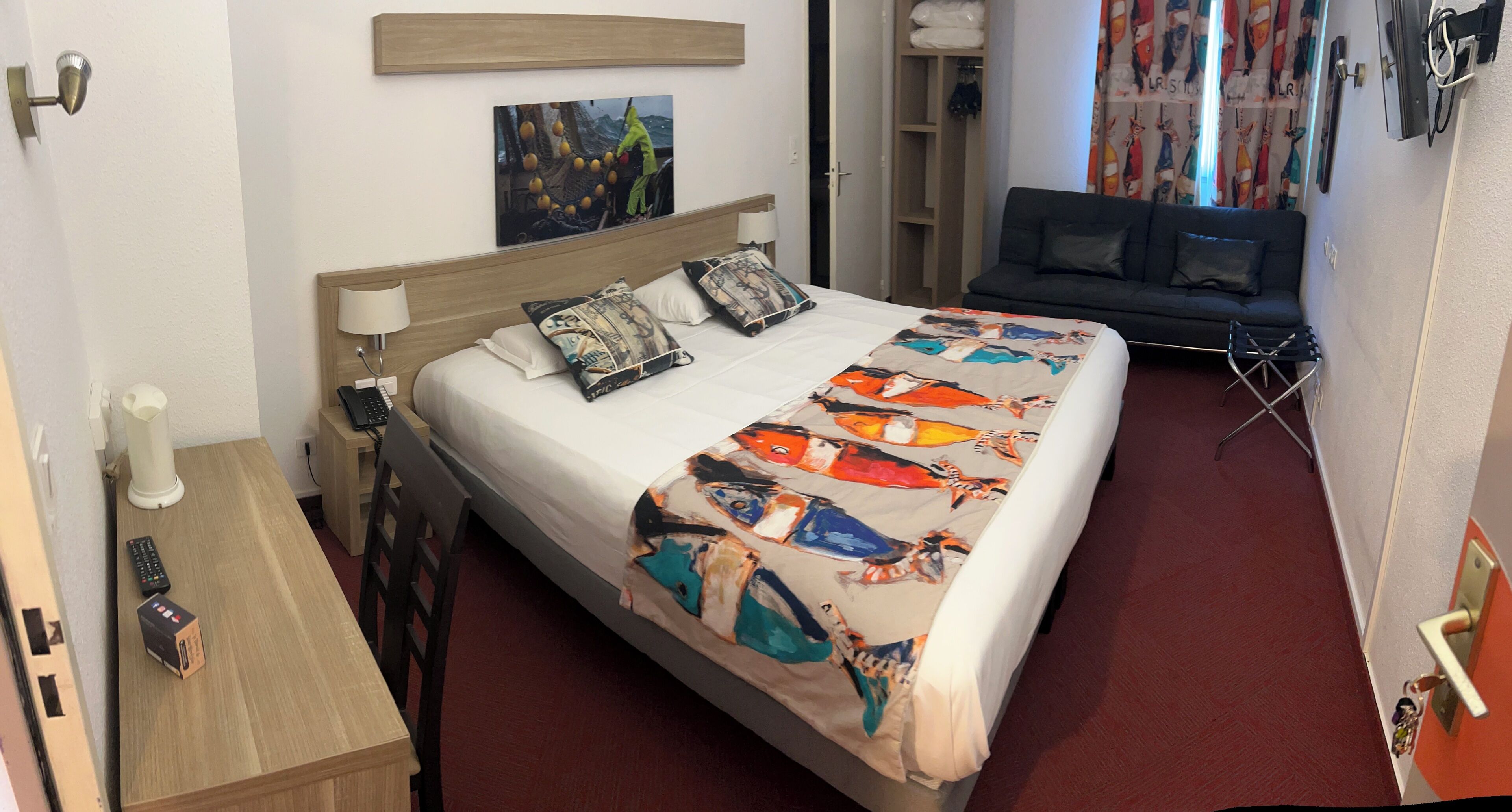 A hotel room with a bed, bedside table, lamp, and a painting on the wall.
