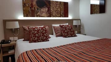 Una habitación de hotel con una cama grande, dos lámparas de noche y un tapiz decorativo sobre la cama.