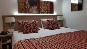 A hotel room with a large bed, two bedside lamps, and a patterned wall hanging above the bed. - Contact Hotel Utah Beach Carentan (Carentan les Marais)