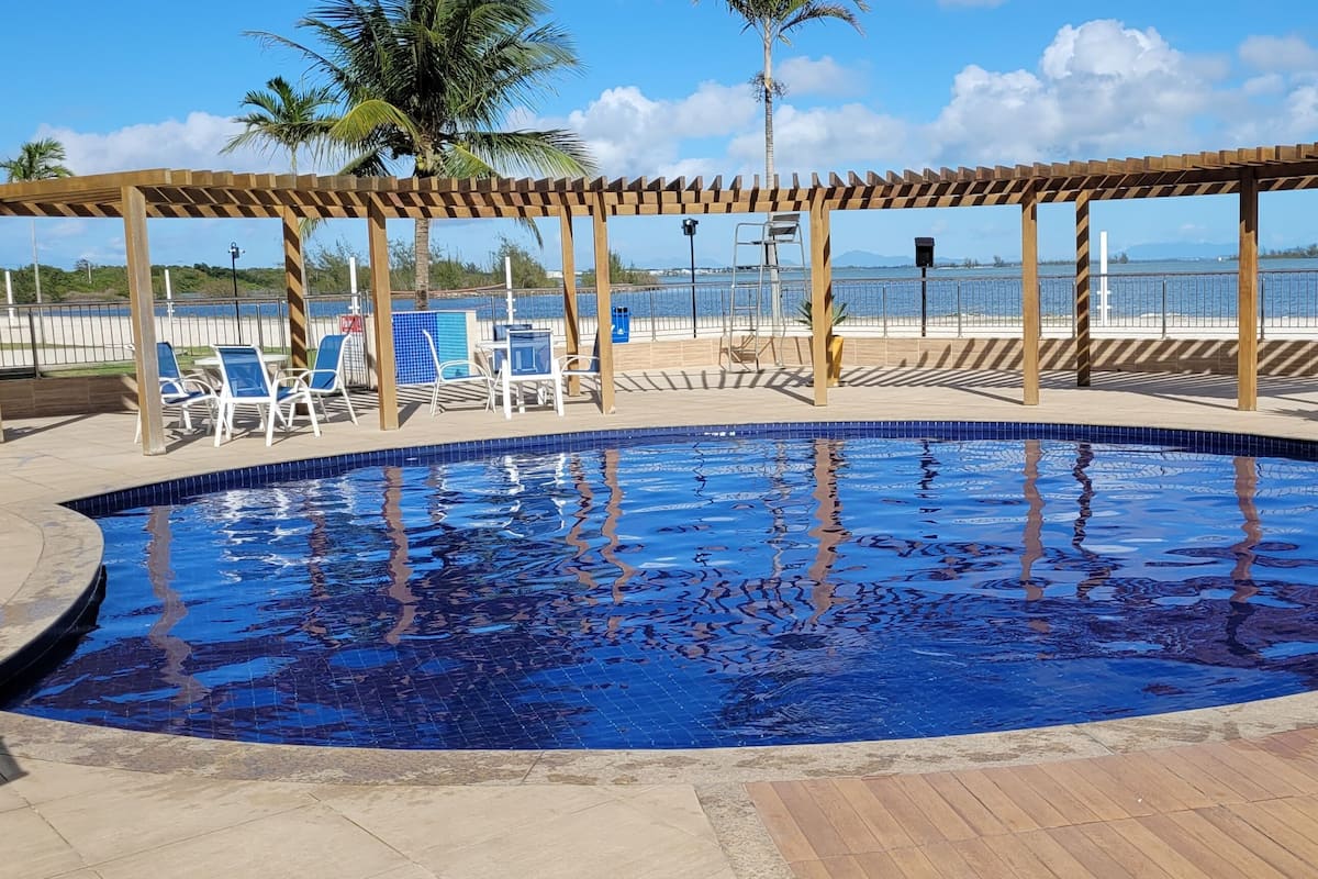 Ein Poolbereich mit einer Holzpergola, Liegestühlen und Blick auf den Strand.